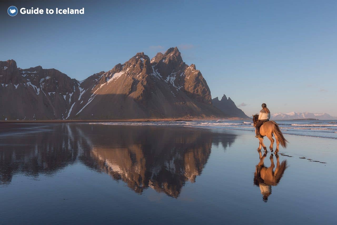 A rider on an Icelandic horse crosses the wet black sand below Vestrahorn mountain at Stokksnes, southeast Iceland.