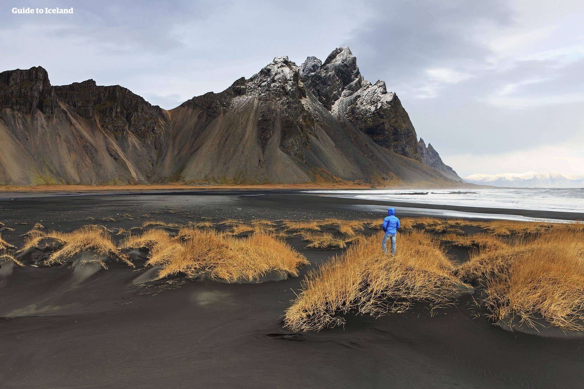 A lone traveller stands on the black-sand beach beneath the dramatic Vestrahorn massif at Stokksnes, southeast Iceland.