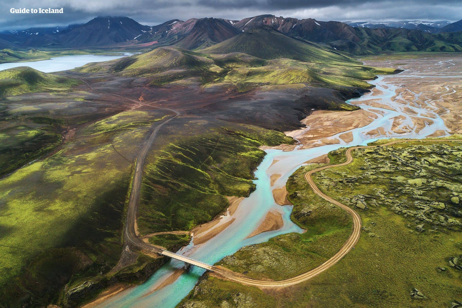 A turquoise river winds past a lava field and rolling mountains in Landmannalaugar, southern Highlands of Iceland.