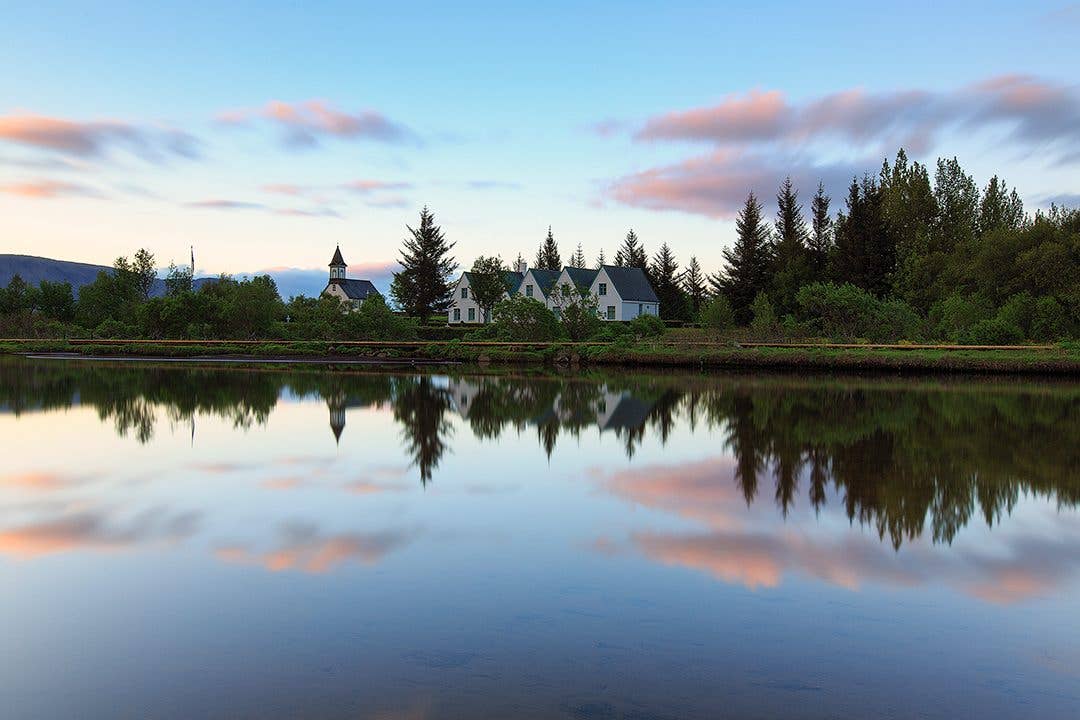 The church at Þingvellir and its houses reflect in still water at sunset in Þingvellir National Park on the Golden Circle, Icela