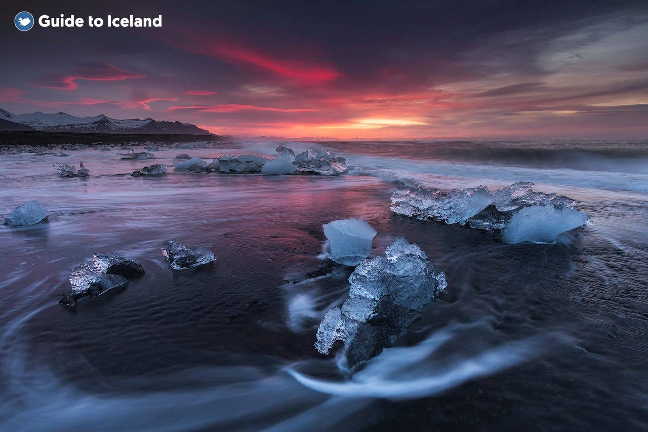 Ice diamonds rest on black sand under a pink dawn sky at Diamond Beach beside Jökulsárlón glacier lagoon, southeast Iceland.