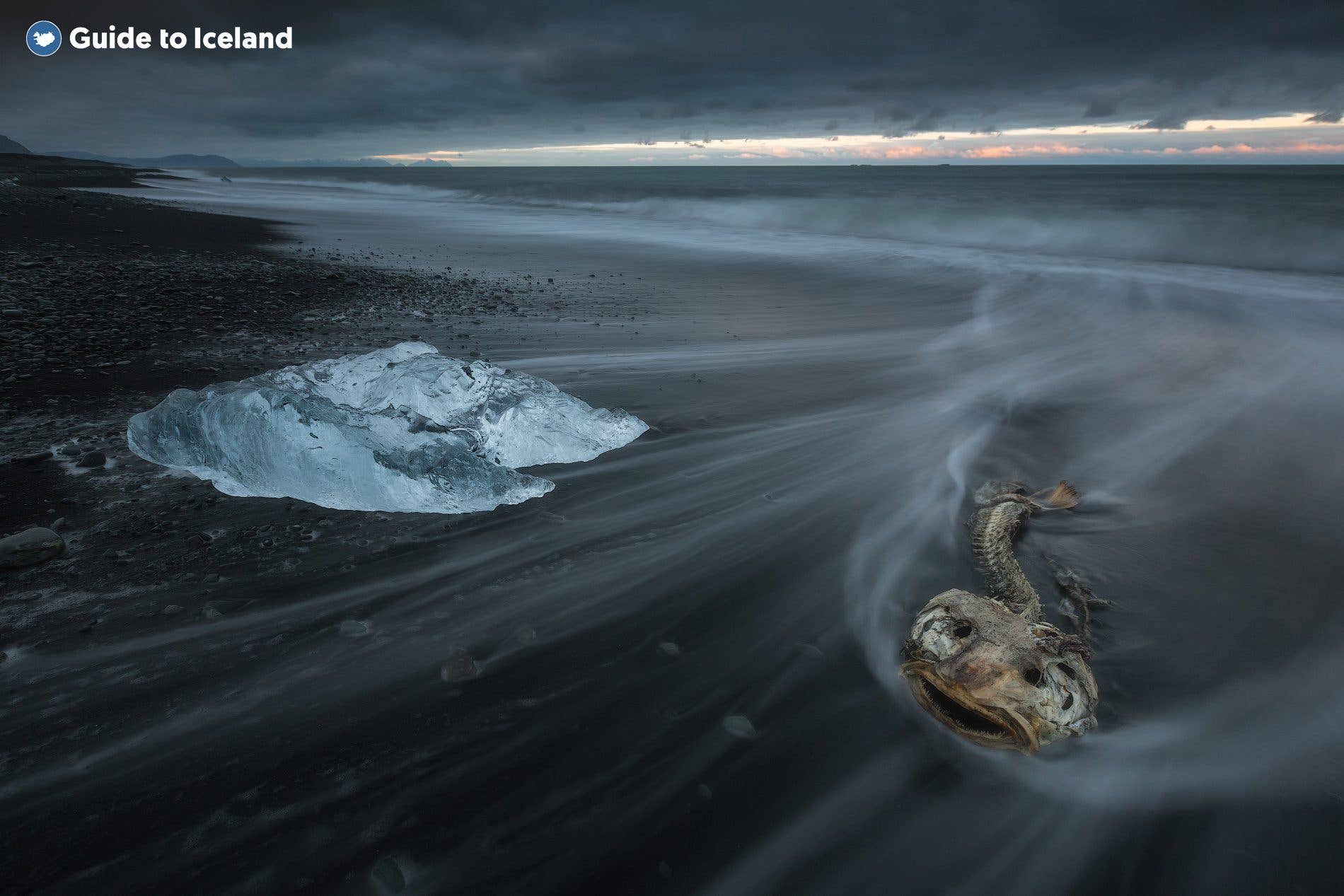 A single glassy iceberg sits on the black sand as a wave recedes at Diamond Beach near Jökulsárlón, southeast Iceland.