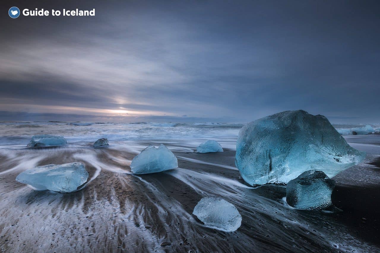 A large blue iceberg sits on the black-sand shore of Diamond Beach near Jökulsárlón glacier lagoon, southeast Iceland.