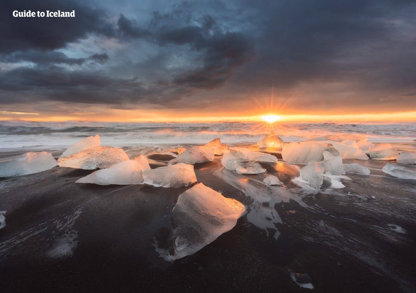 The sun sets over ice scattered across the black sand of Diamond Beach near Jökulsárlón glacier lagoon, Iceland.