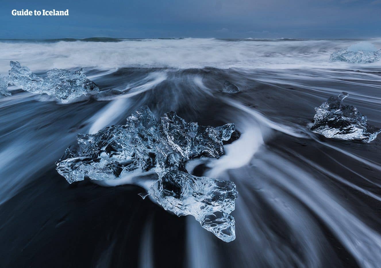 Waves stream around a jagged block of glacier ice on Diamond Beach beside Jökulsárlón, southeast Iceland.