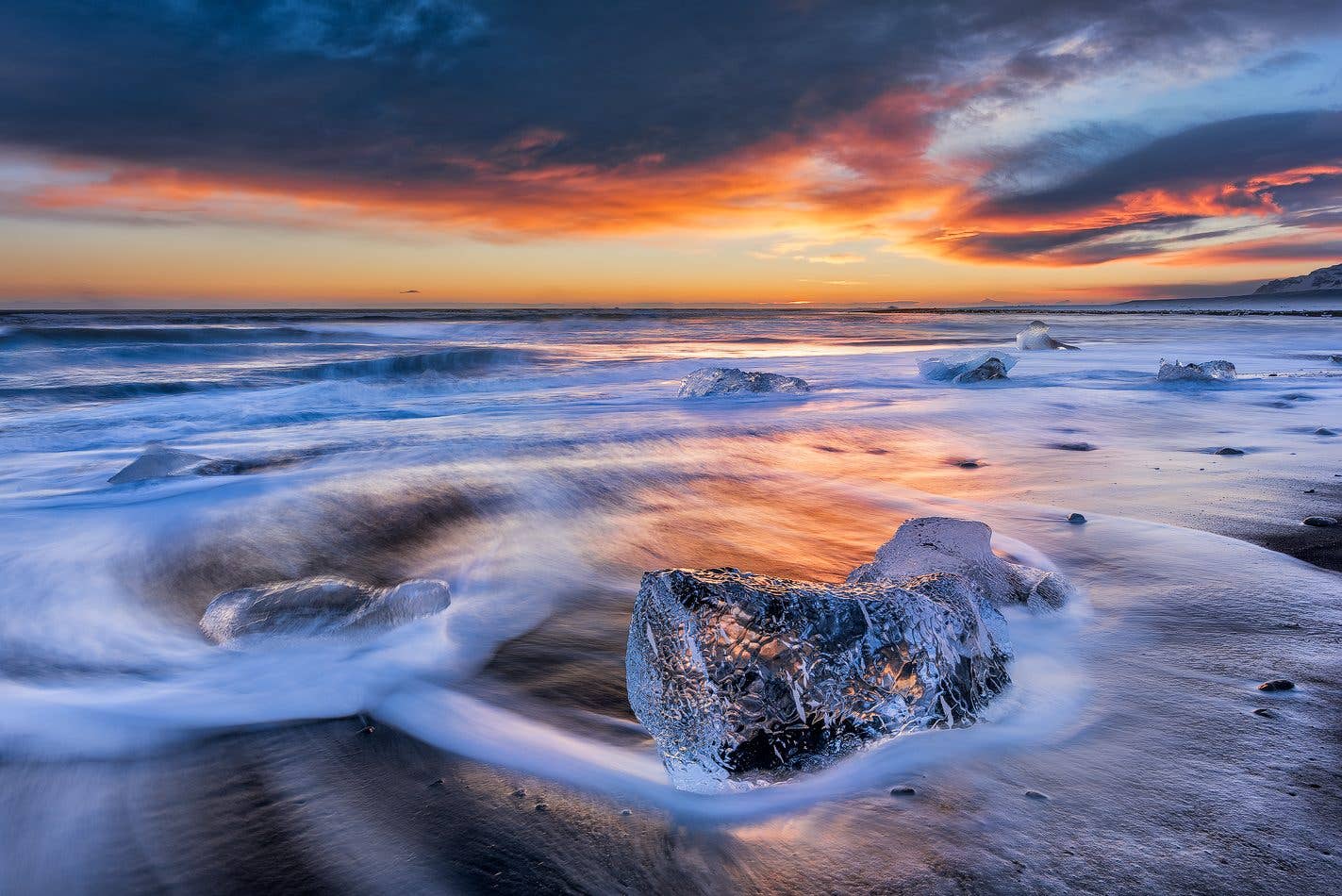 Icebergs glow under a fiery sunset on the black sand of Diamond Beach near Jökulsárlón glacier lagoon, Iceland.