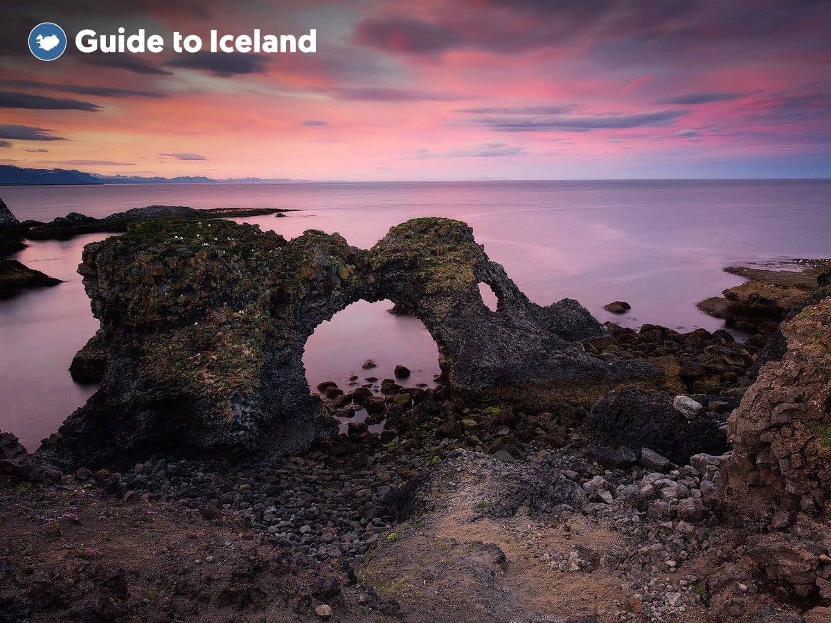 The Gatklettur stone arch frames a pink summer sunset along the rugged coast at Arnarstapi on the Snæfellsnes Peninsula, West Ic