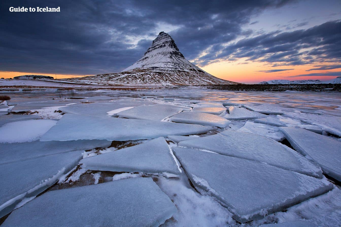 Kirkjufell mountain rises beyond a lake broken into sheets of ice at sunset on the Snæfellsnes Peninsula, West Iceland.