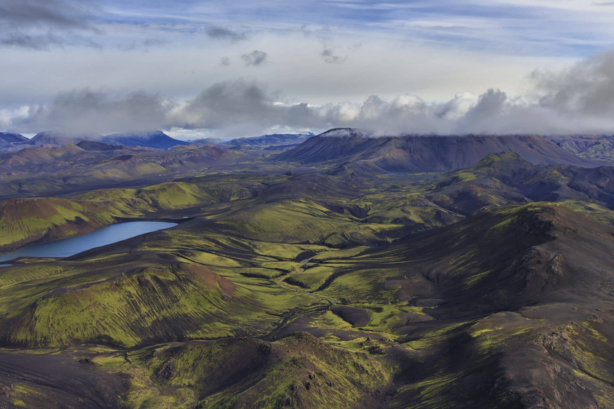 An aerial view of green mossy hills, lakes and glacial valleys stretching across the Icelandic Highlands.