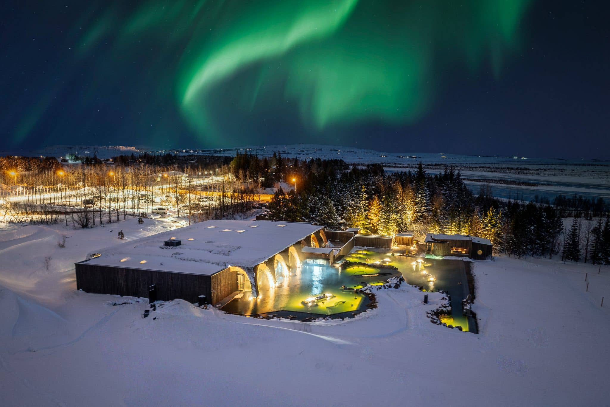 The northern lights glow above a geothermal lagoon lit up in the snow, seen from the air in Iceland.