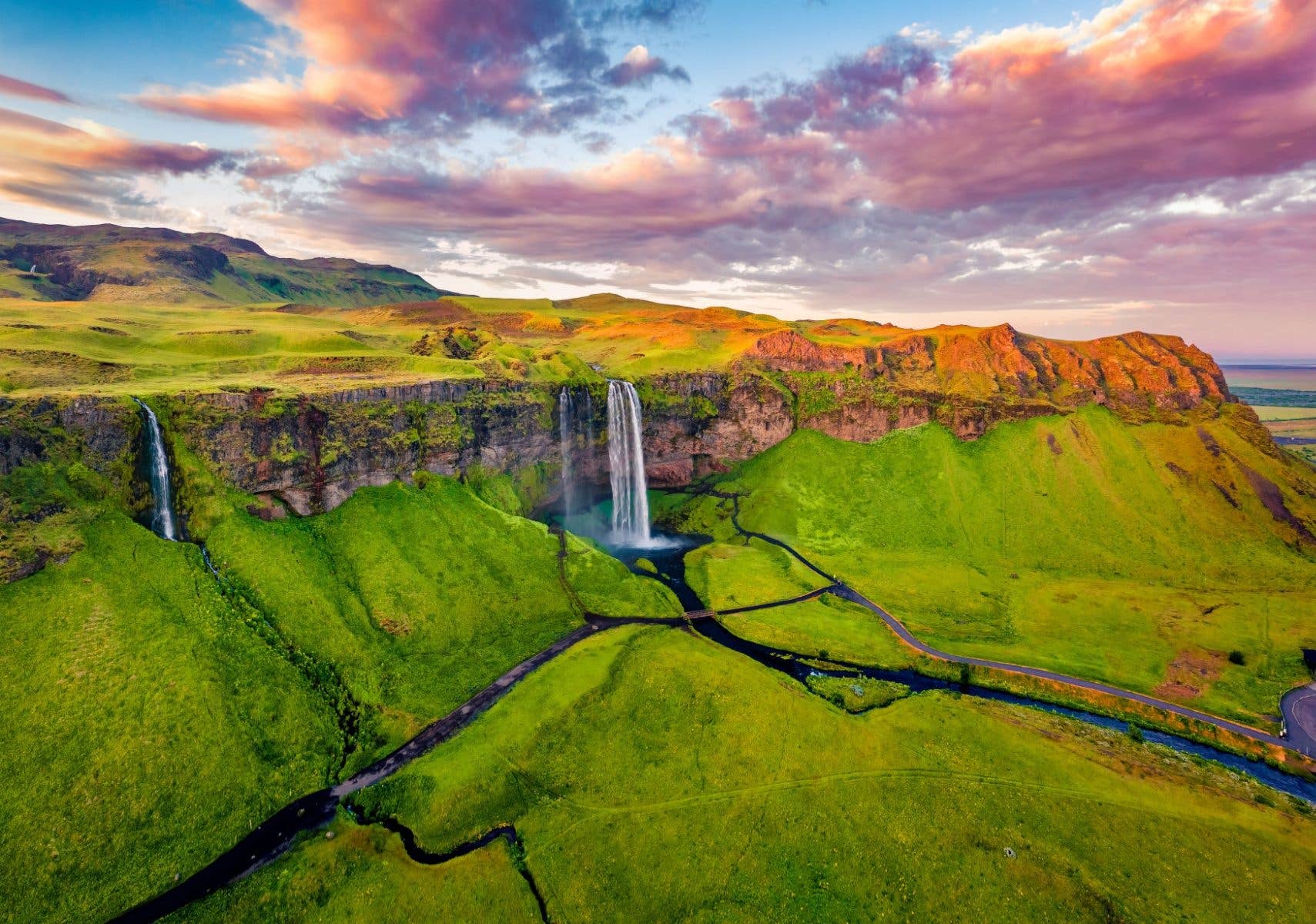 An aerial view of Seljalandsfoss waterfall tumbling over green cliffs at sunset on Iceland's south coast.
