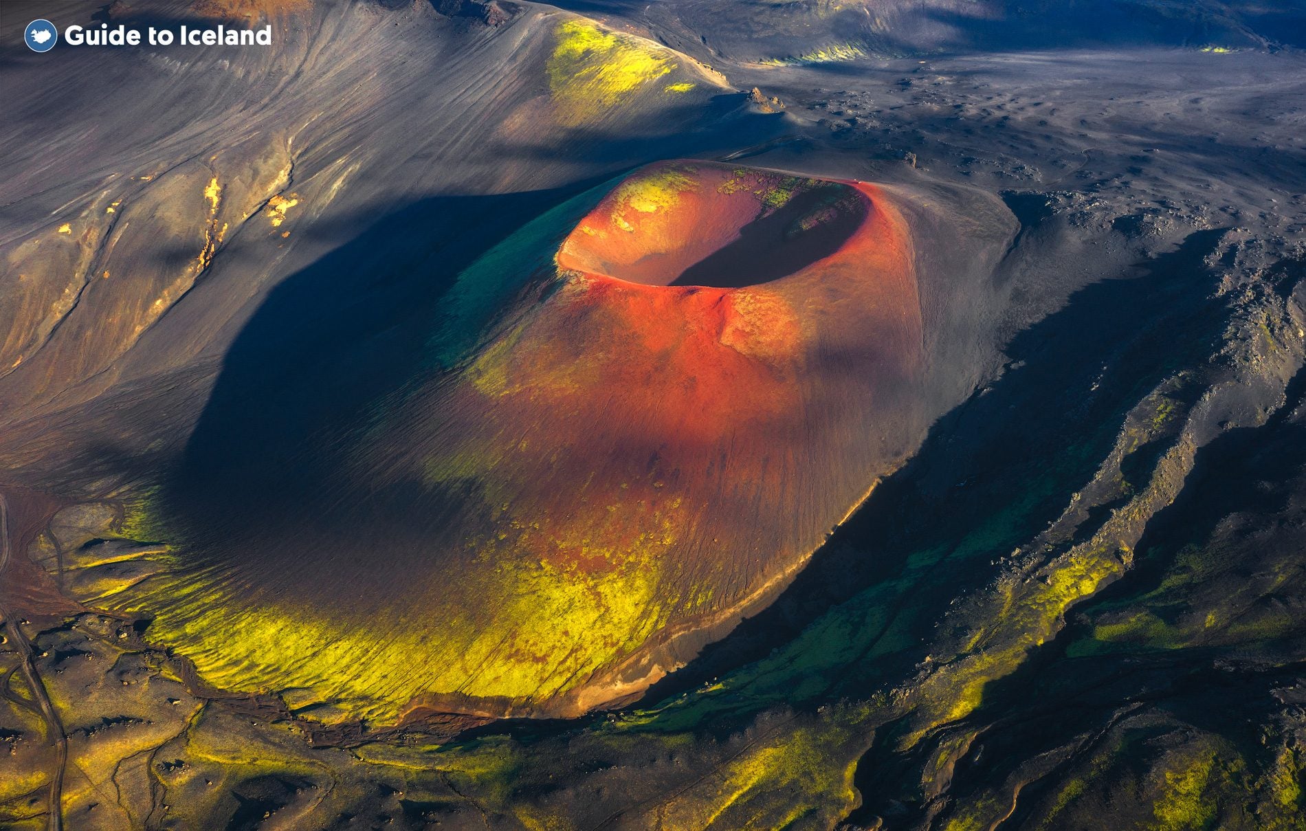 A deep volcanic crater glows red and gold beside green moss in the Landmannalaugar area of the Highlands, Iceland.