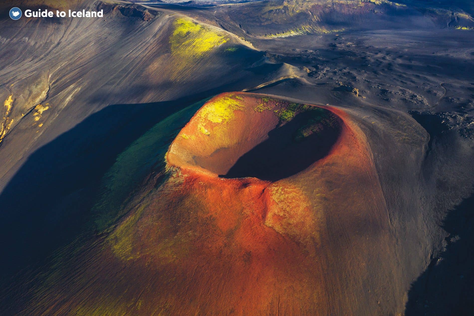 A green-and-red scoria crater cone rises from the volcanic landscape of the Icelandic Highlands.