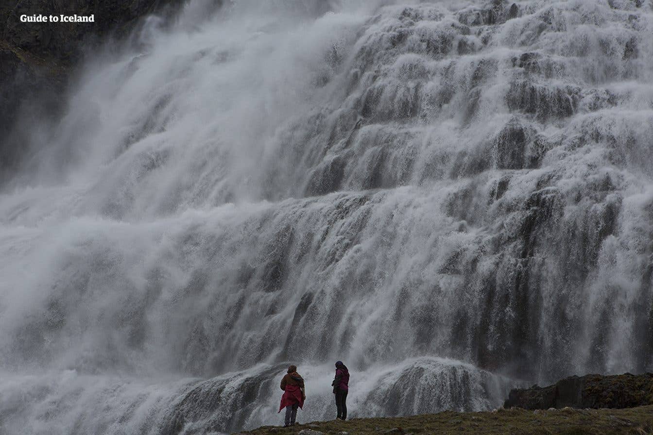 Two visitors stand at the foot of the tiered Dynjandi waterfall, the largest in the Westfjords of Iceland.
