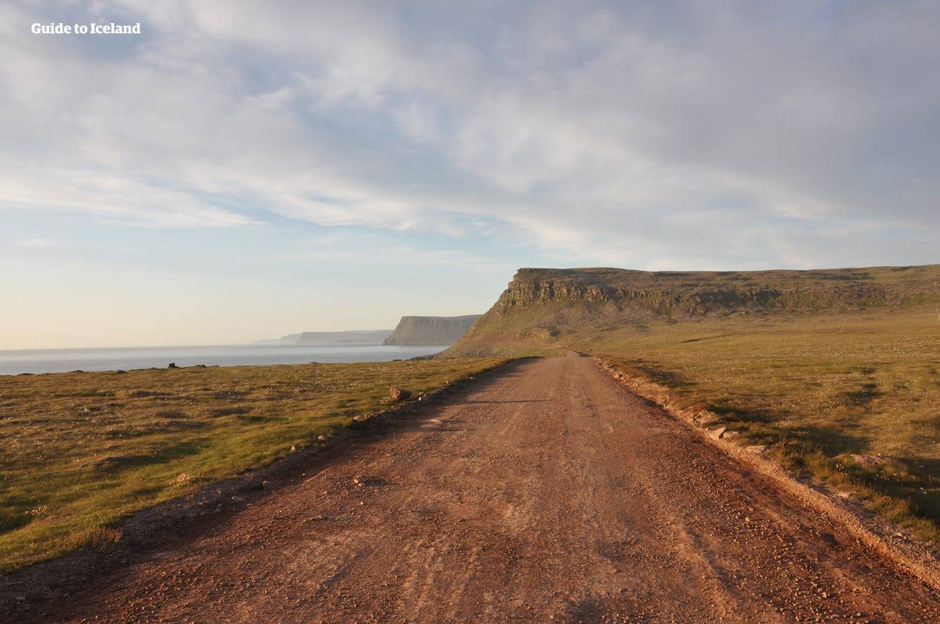 A gravel road runs beside the sea below a flat-topped mountain in the Westfjords of Iceland.