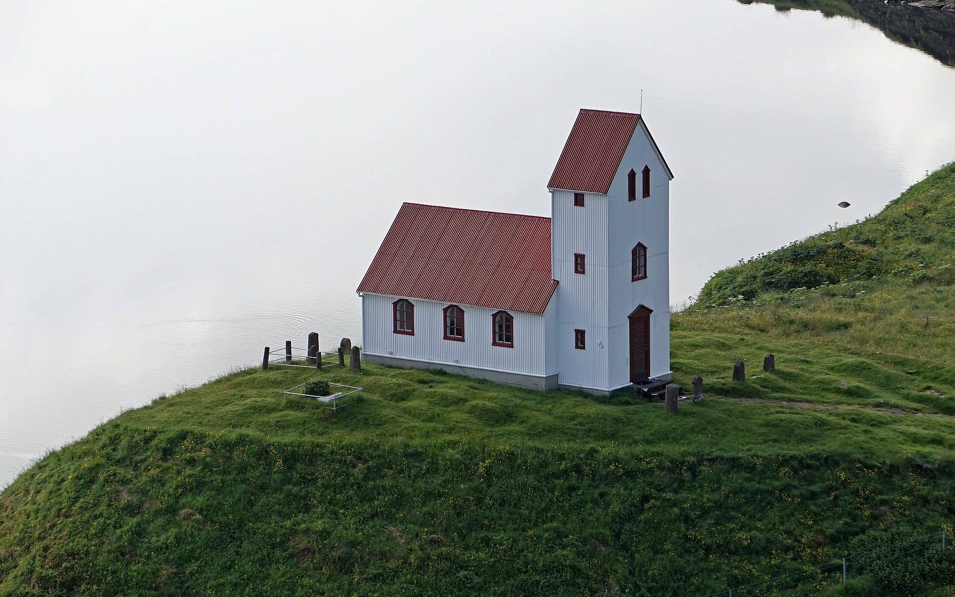 The white, red-roofed Úlfljótsvatn church stands on a green hill by the lake in southwest Iceland.
