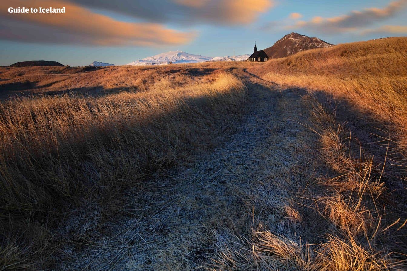 A frosty path leads toward the black Búðakirkja church with Snæfellsjökull glacier beyond, West Iceland.