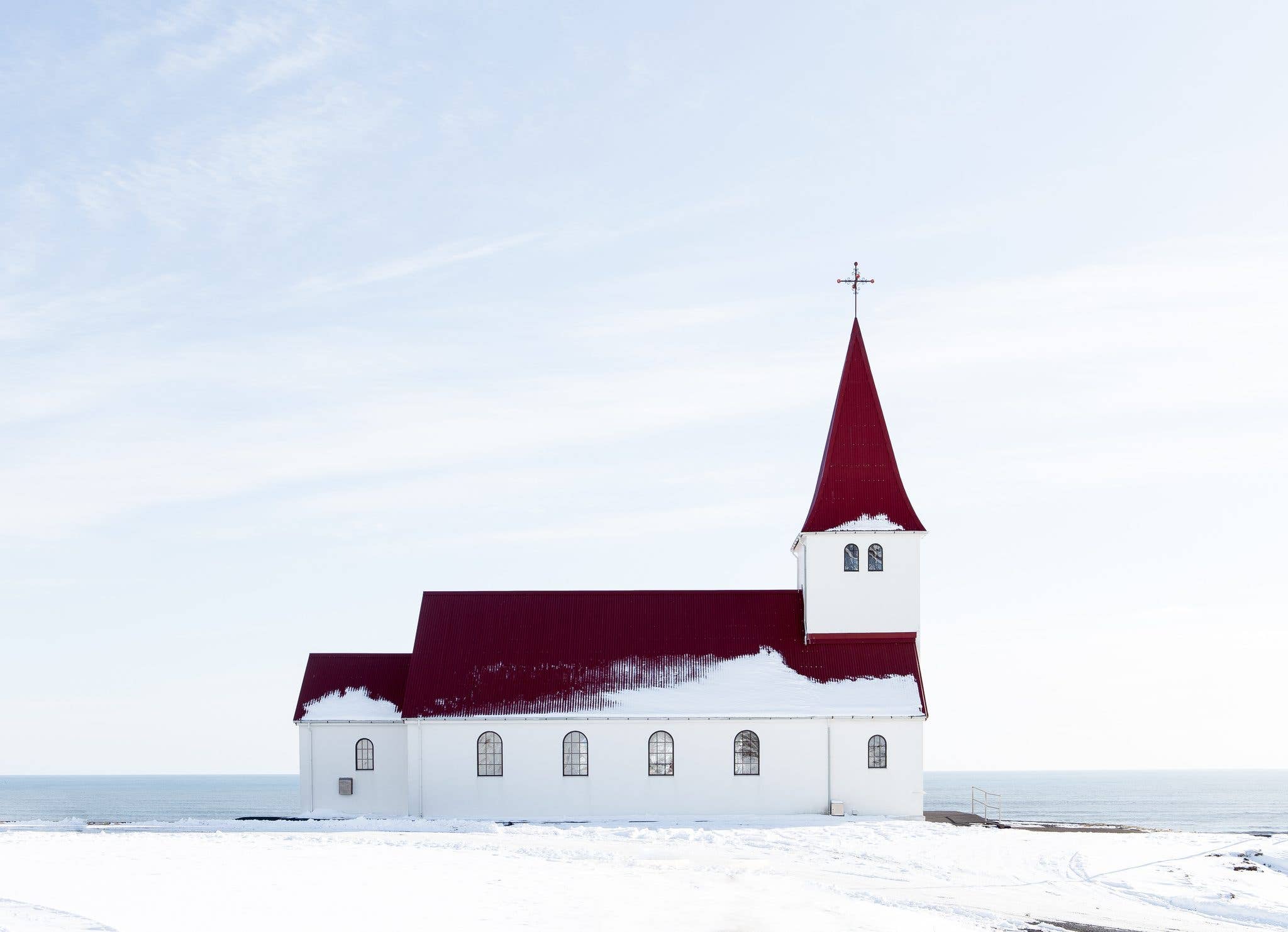 The red-roofed Víkurkirkja church stands in the snow above the village of Vík in South Iceland.