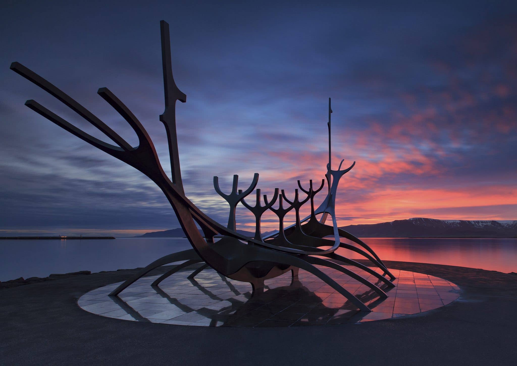 The Sun Voyager (Sólfarið) steel sculpture sits by the sea against a colourful sunset in Reykjavík, Iceland.