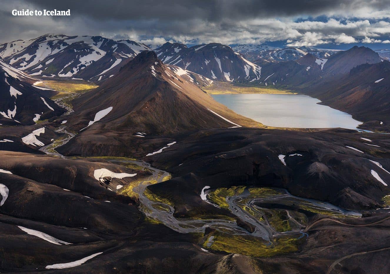 A winding track passes a Highland lake among dark volcanic mountains in the Fjallabak area of Iceland.
