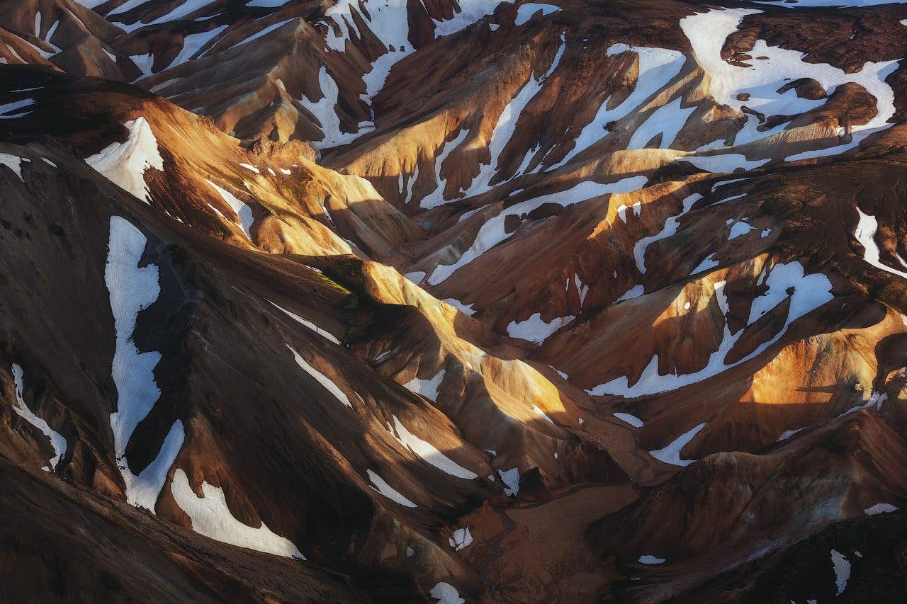 Low sun lights the rust-coloured, snow-streaked mountains of Fjallabak in the Icelandic Highlands.