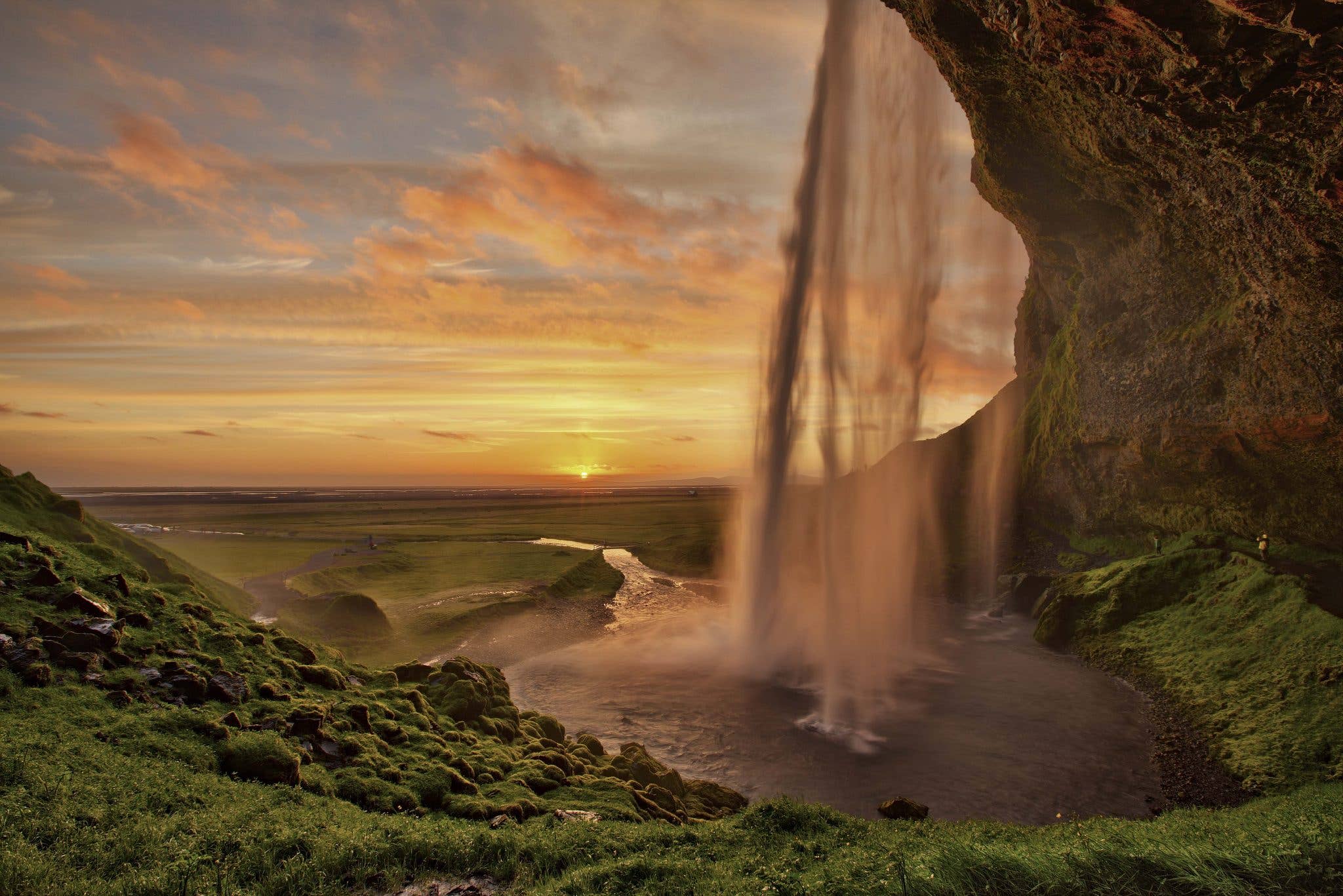 The midnight sun sets behind Seljalandsfoss, the waterfall you can walk behind, in South Iceland.