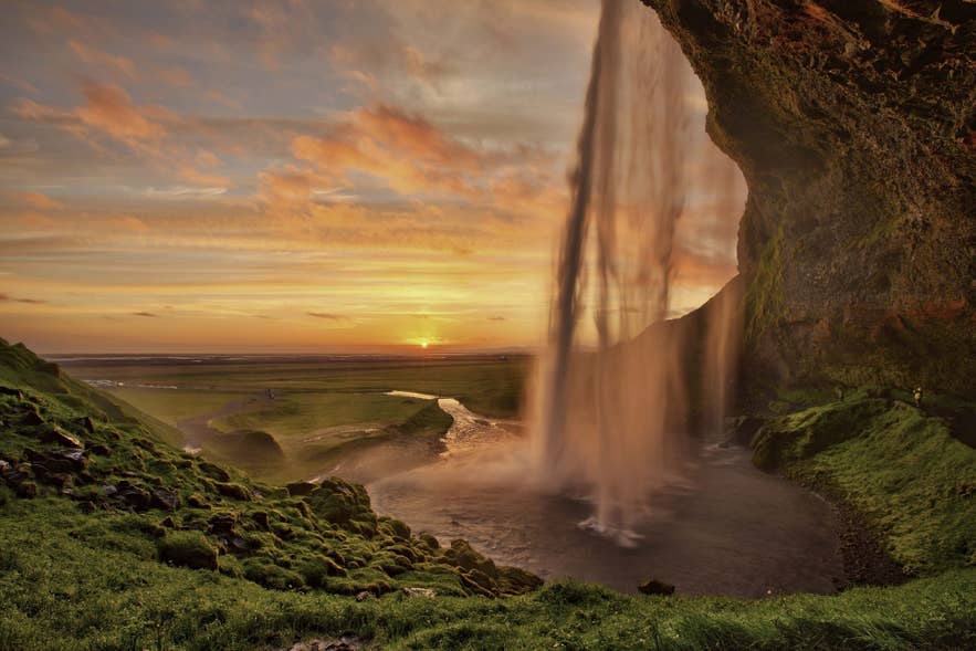 The midnight sun sets behind Seljalandsfoss waterfall in South Iceland in summer