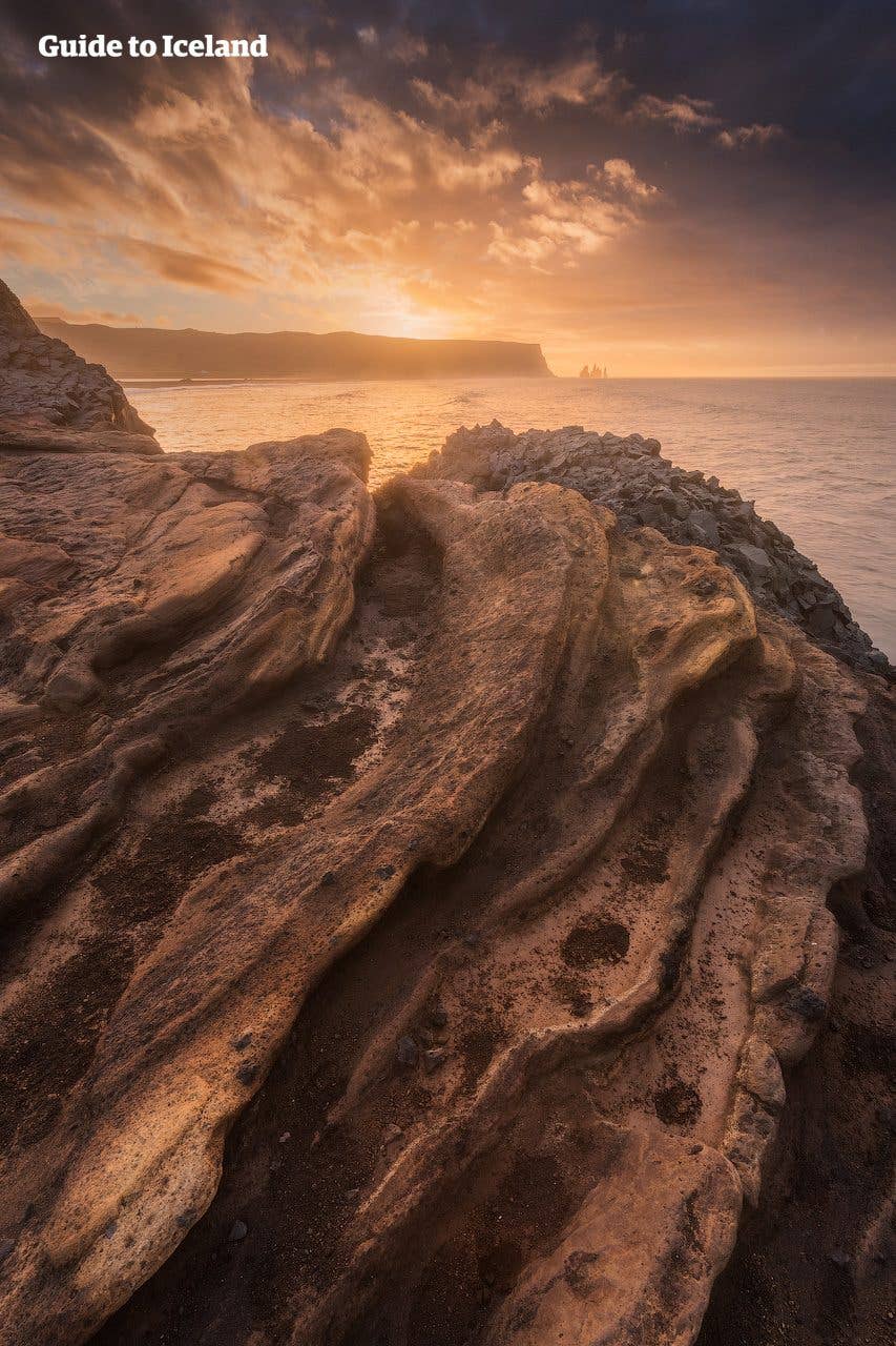 Sunset light rakes across the rocks above Reynisfjara black-sand beach on the south coast of Iceland.