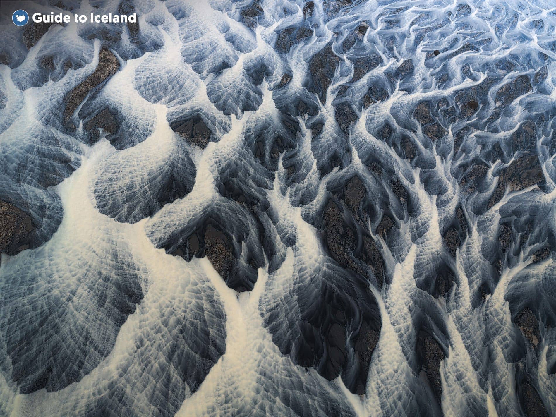 Glacial rivers braid into intricate patterns across the black Highland sands of Iceland in summer.