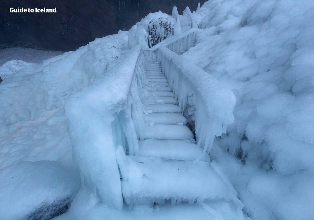 An ice-covered stairway climbs beside the frozen spray of Seljalandsfoss waterfall in winter, South Iceland.
