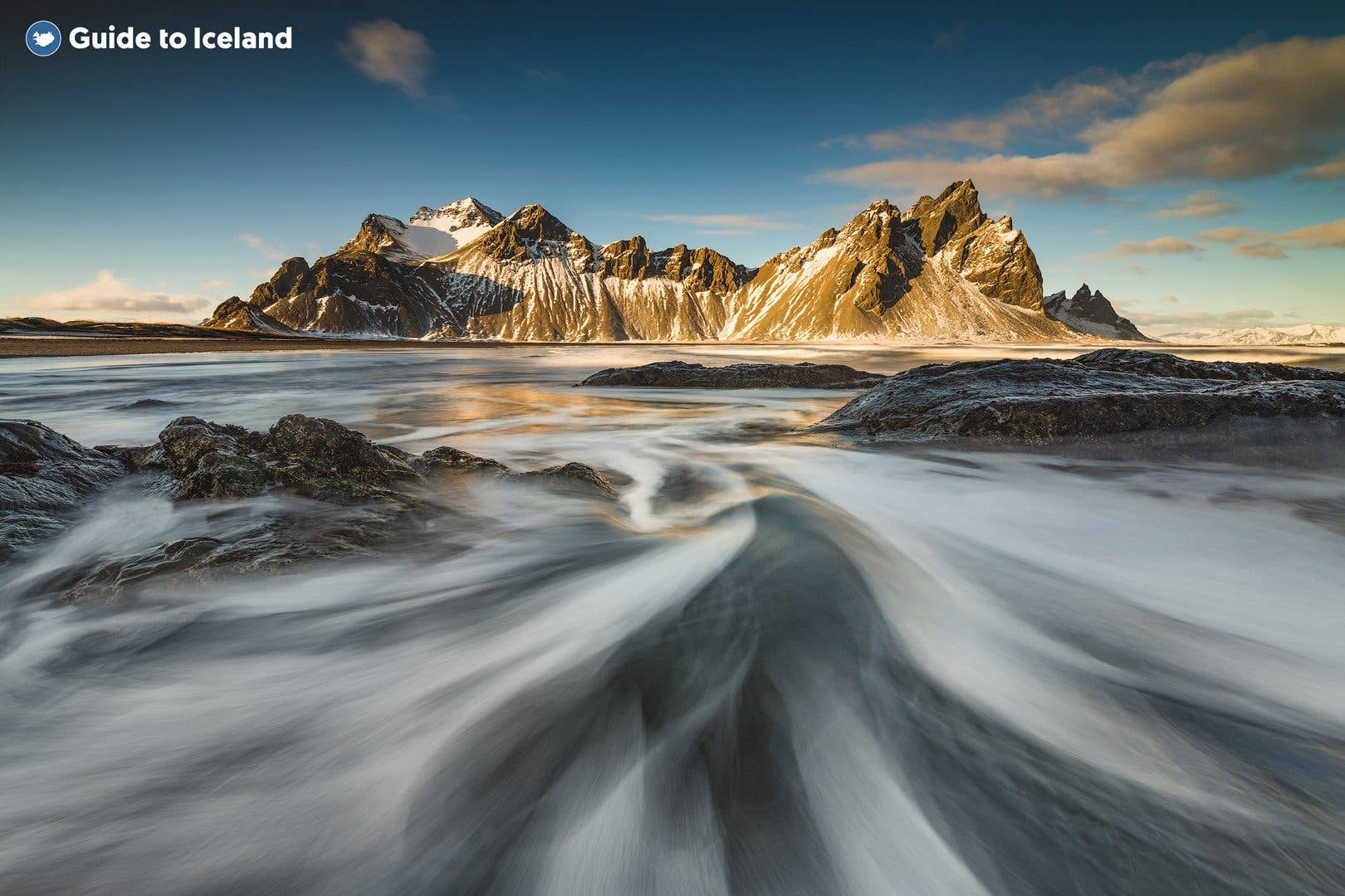 Waves wash over black sand below the snow-capped Vestrahorn mountain at Stokksnes in winter, southeast Iceland.