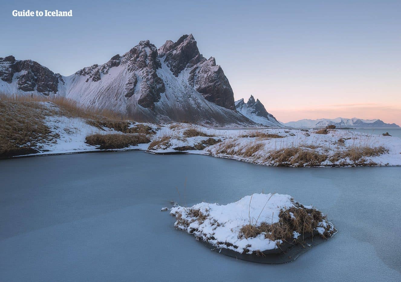 Snow-covered islets dot a still lagoon below Vestrahorn mountain at Stokksnes in winter, southeast Iceland.