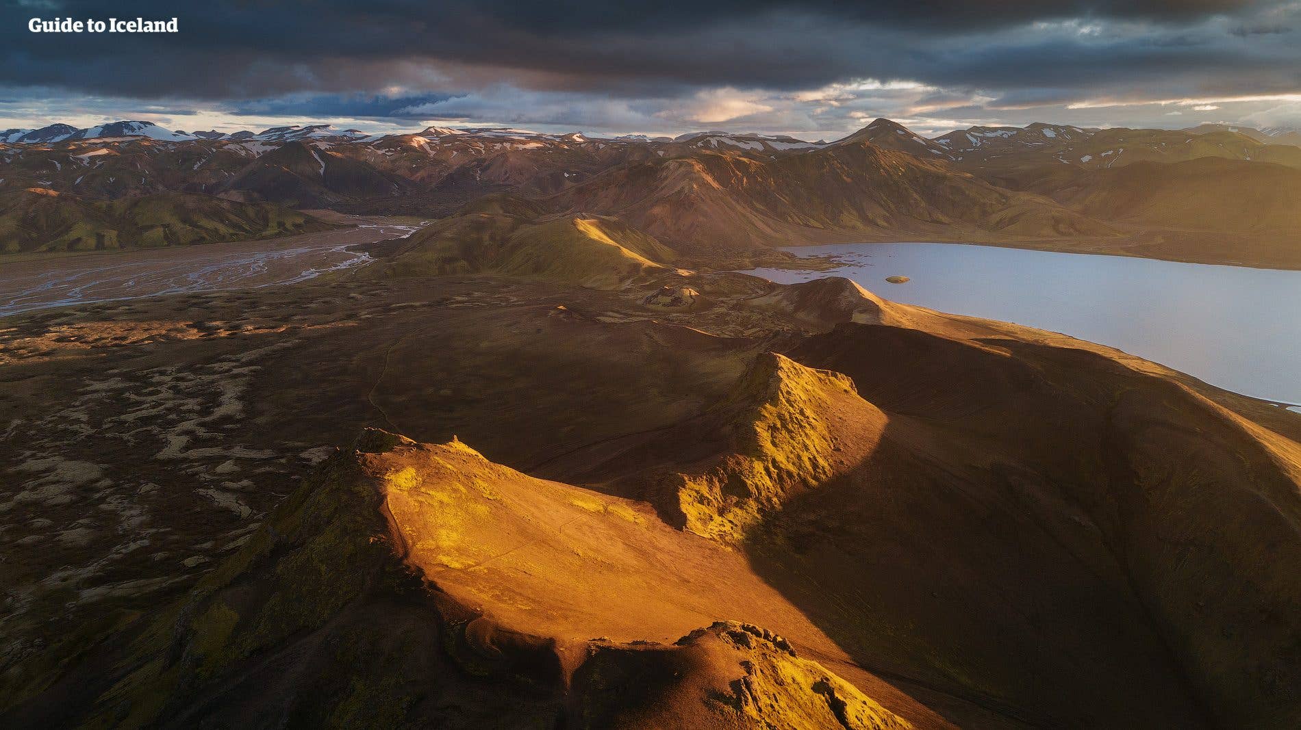 Golden evening light rakes across a volcanic crater rim above a Highland lake in Iceland.
