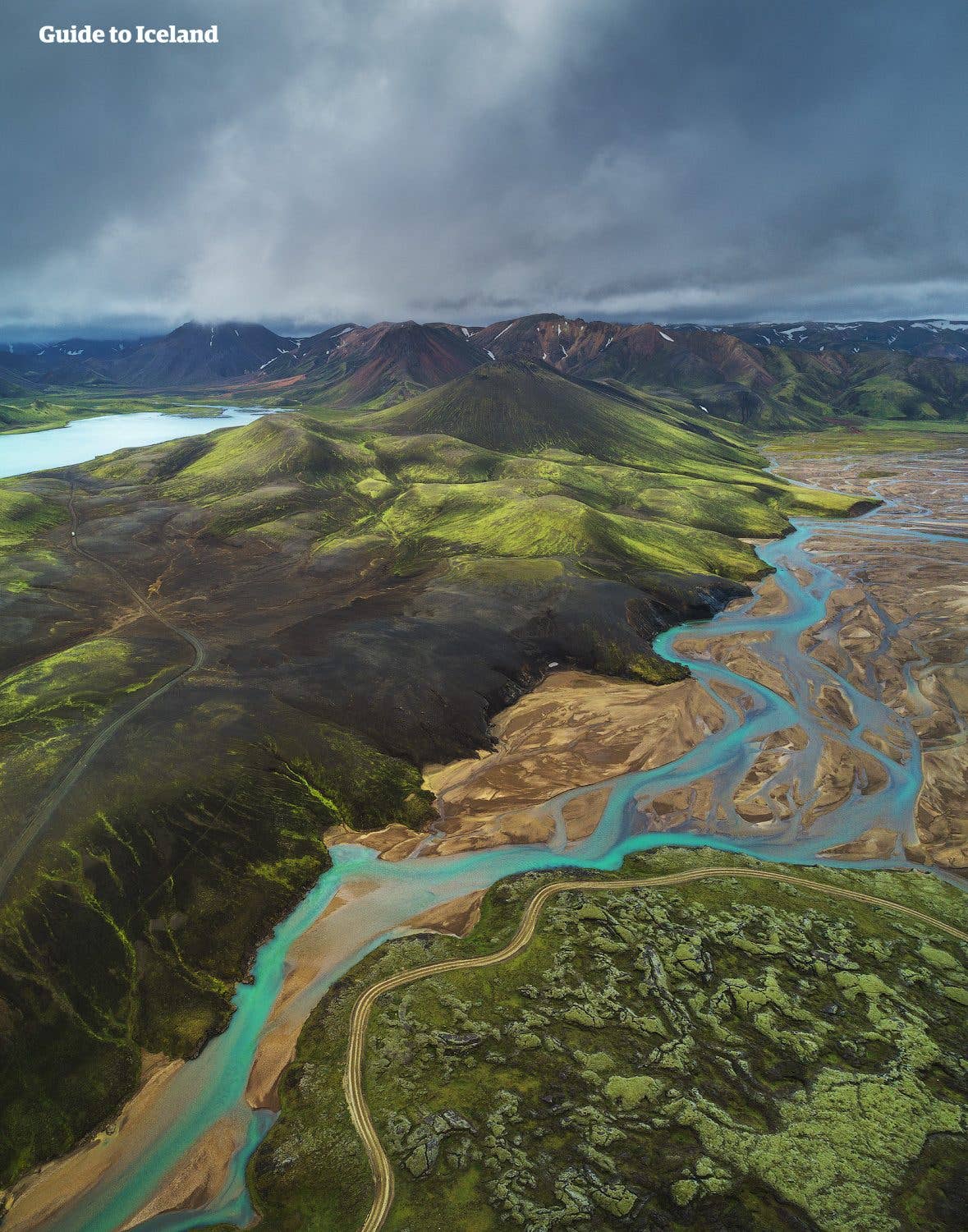 A turquoise glacial river winds past green, moss-covered volcanic hills in the Icelandic Highlands.