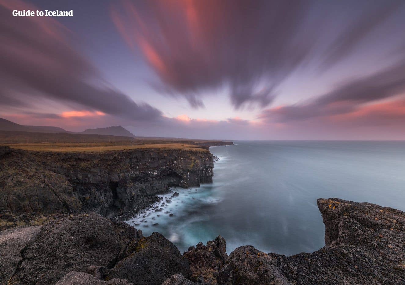 A pink sunset glows over the rugged basalt coastline at Arnarstapi on the Snæfellsnes Peninsula, West Iceland.