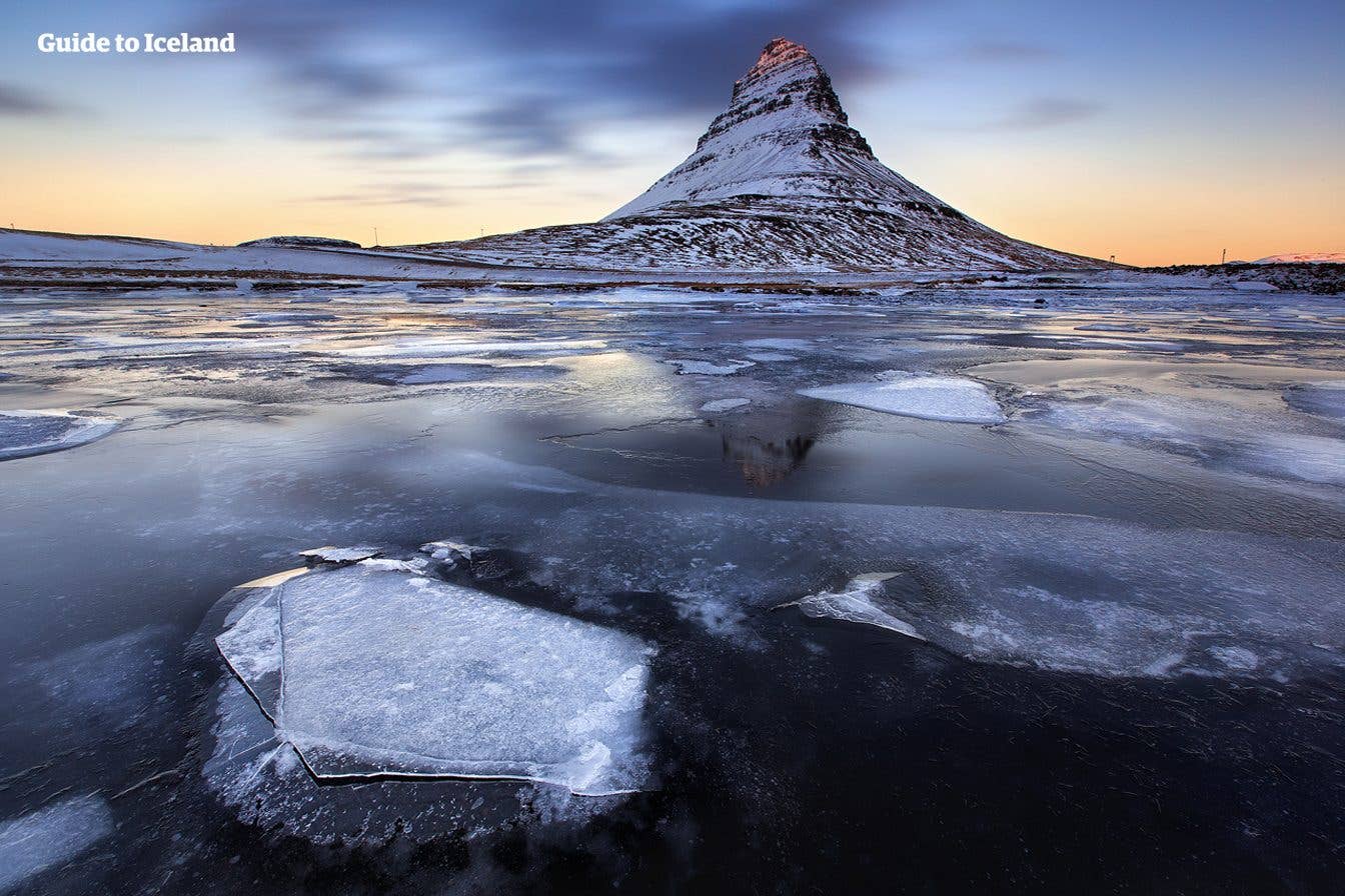 Sheets of ice float on a lagoon below the snow-capped Kirkjufell mountain at sunrise on the Snæfellsnes Peninsula, Iceland.