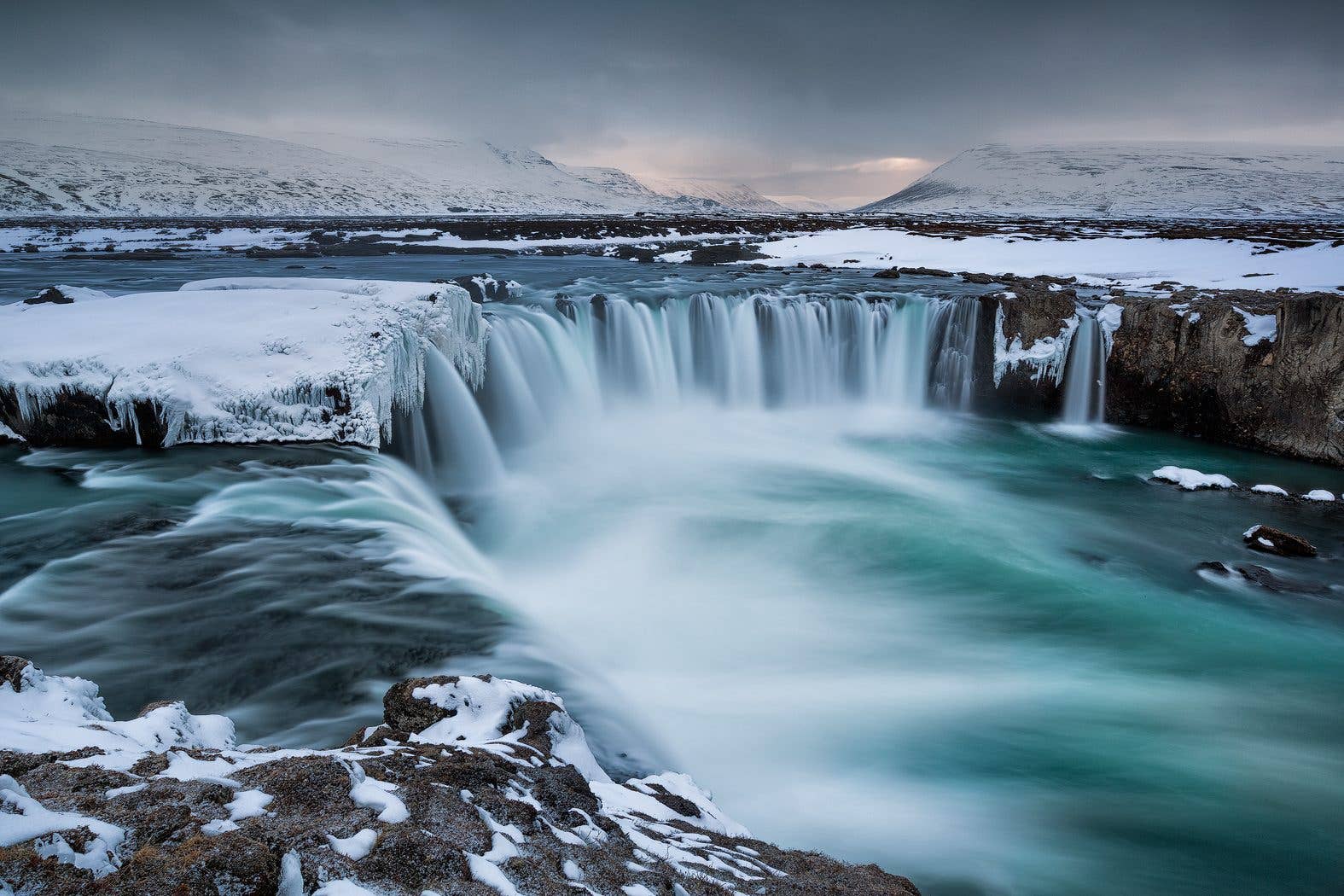 Goðafoss waterfall flows between snow-covered banks in winter in North Iceland.