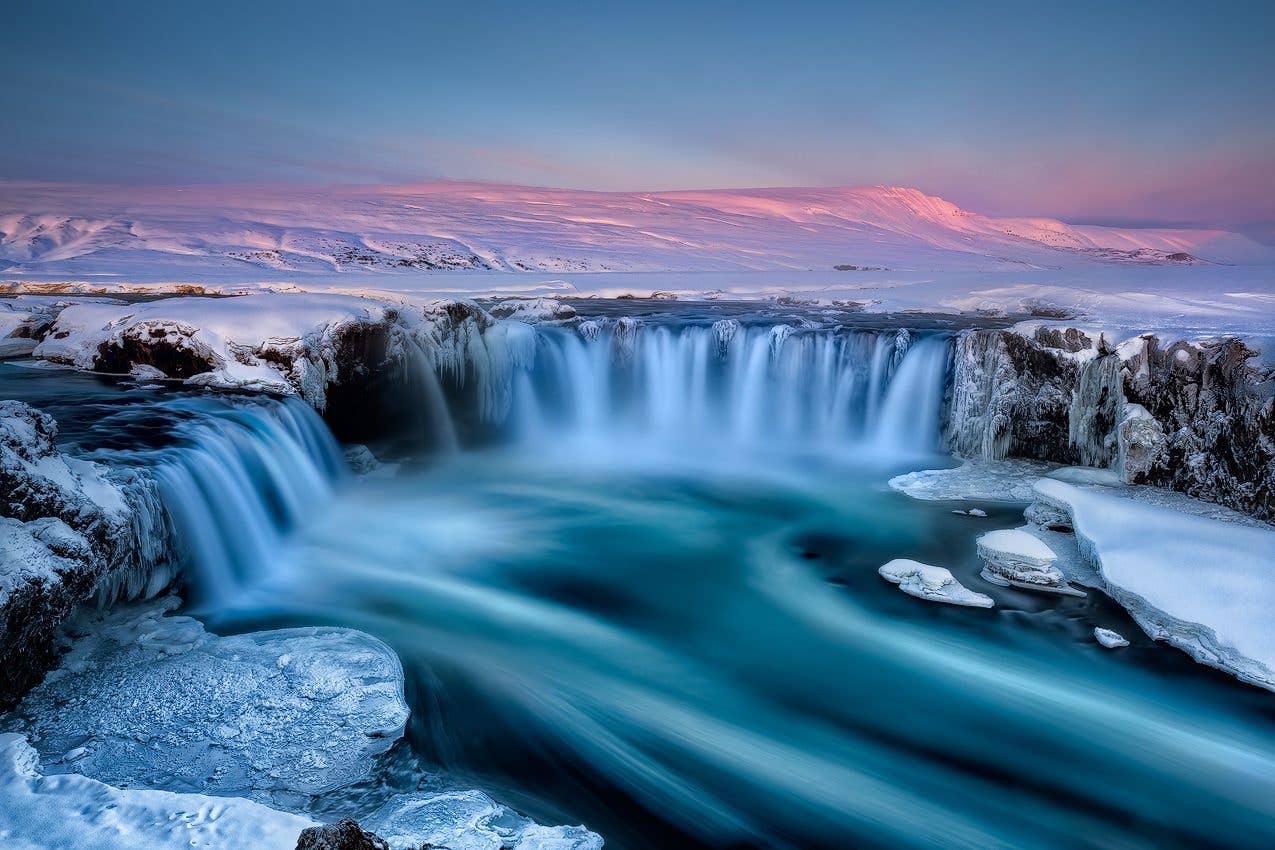 A pink winter dawn colours the sky above the icy Goðafoss waterfall in North Iceland.