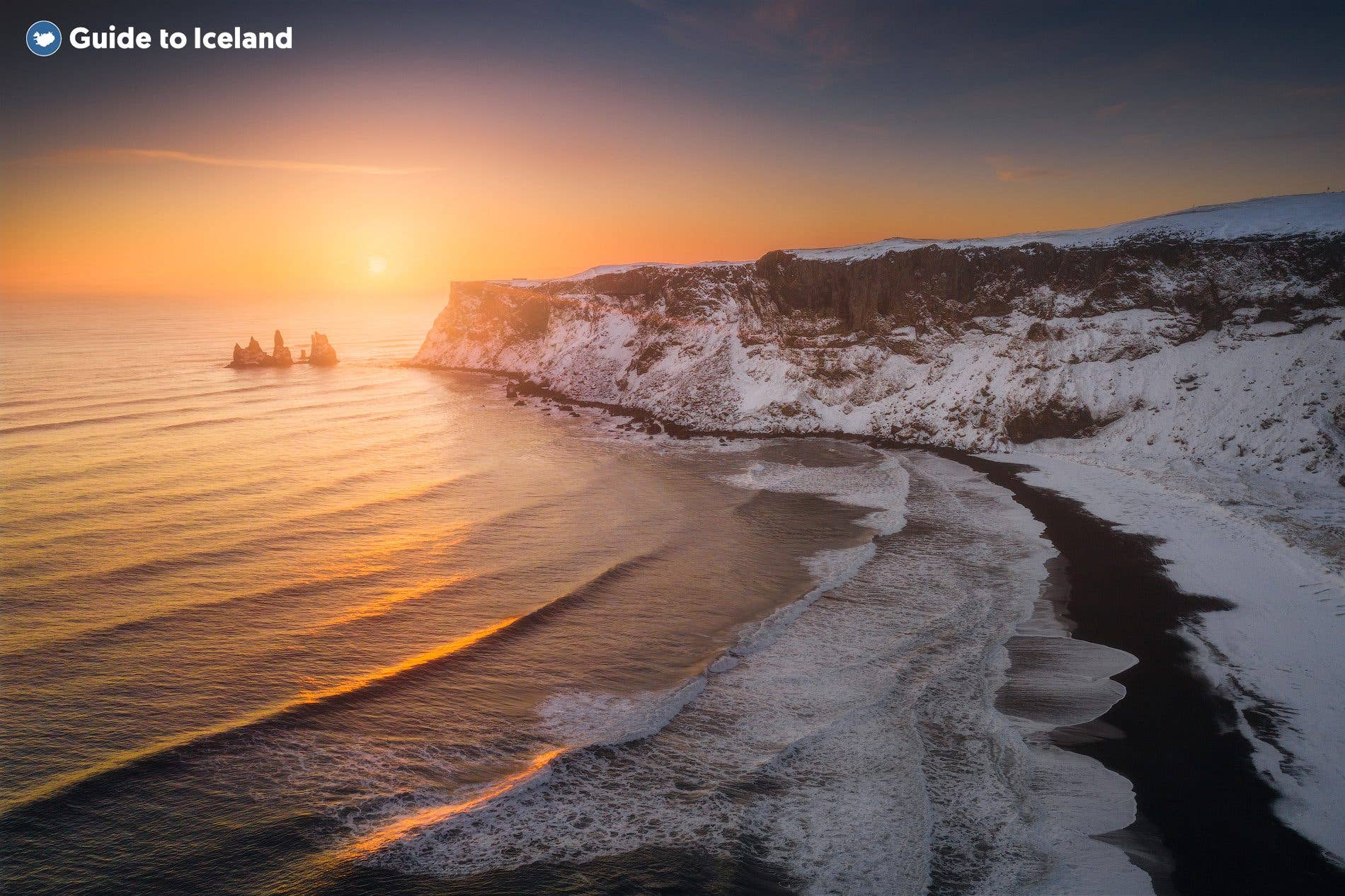 Winter sun lights the snowy cliffs above the black sands and Reynisdrangar sea stacks near Vík, South Iceland.