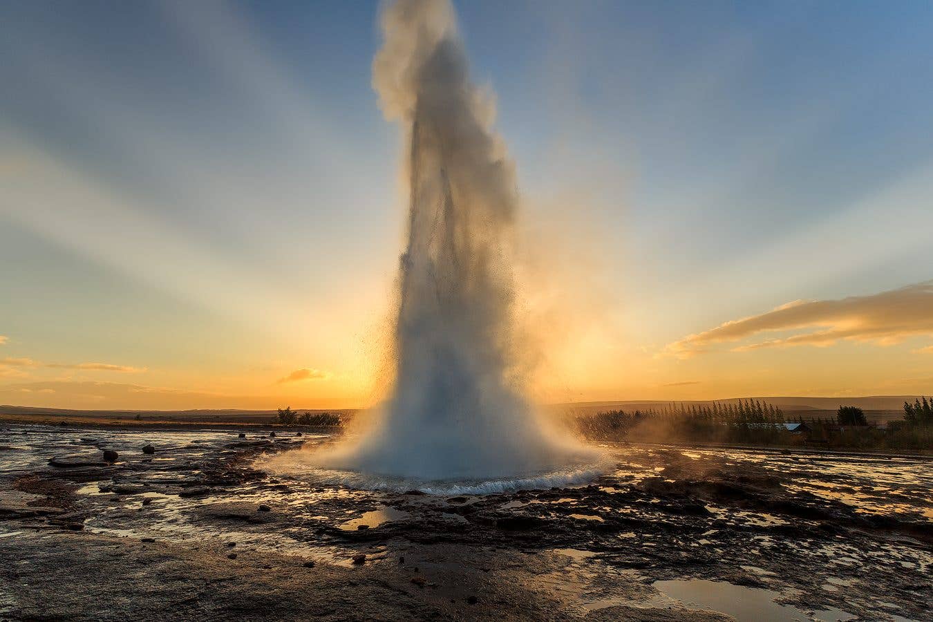 A column of water rises from the Strokkur geyser against a golden sky on the Golden Circle, Iceland.