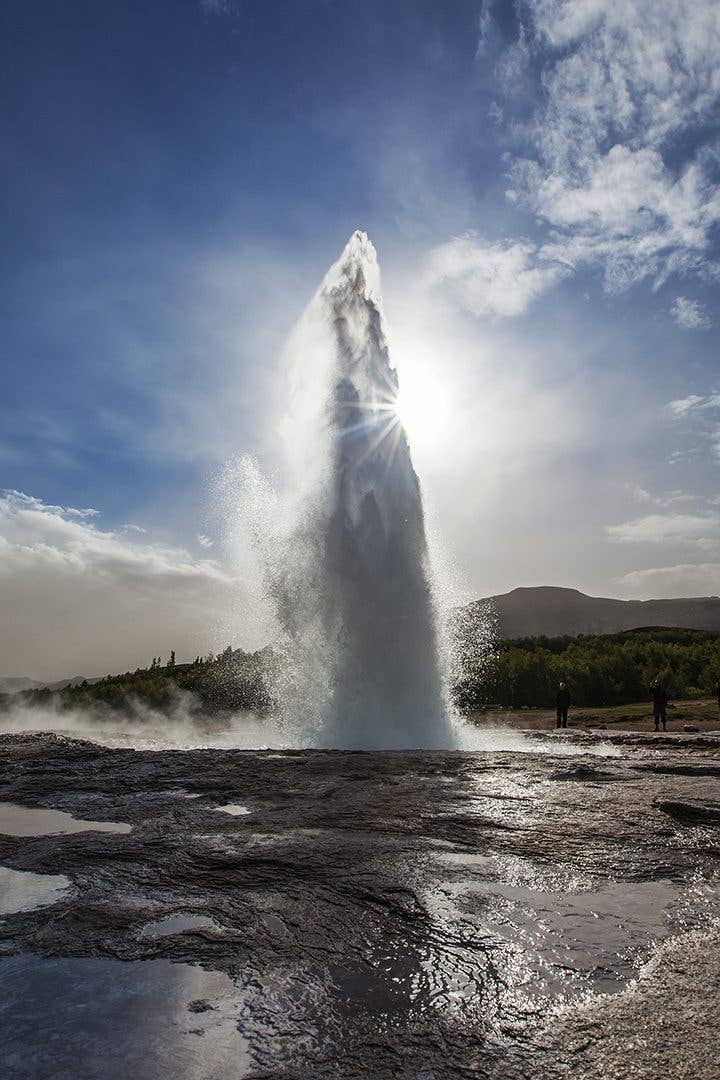 The Strokkur geyser bursts upward, backlit by the sun, in the Geysir area on the Golden Circle, Iceland.
