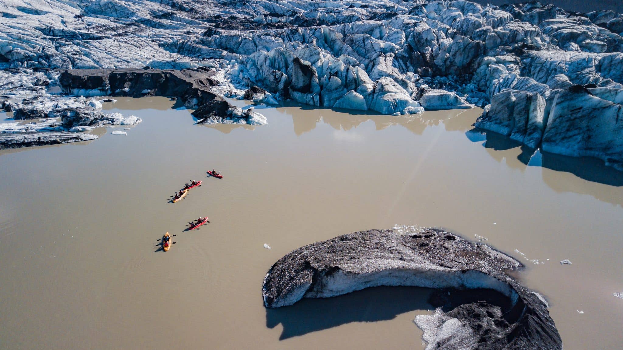Kayakers paddle among icebergs on a glacier lagoon, seen from above in Iceland.