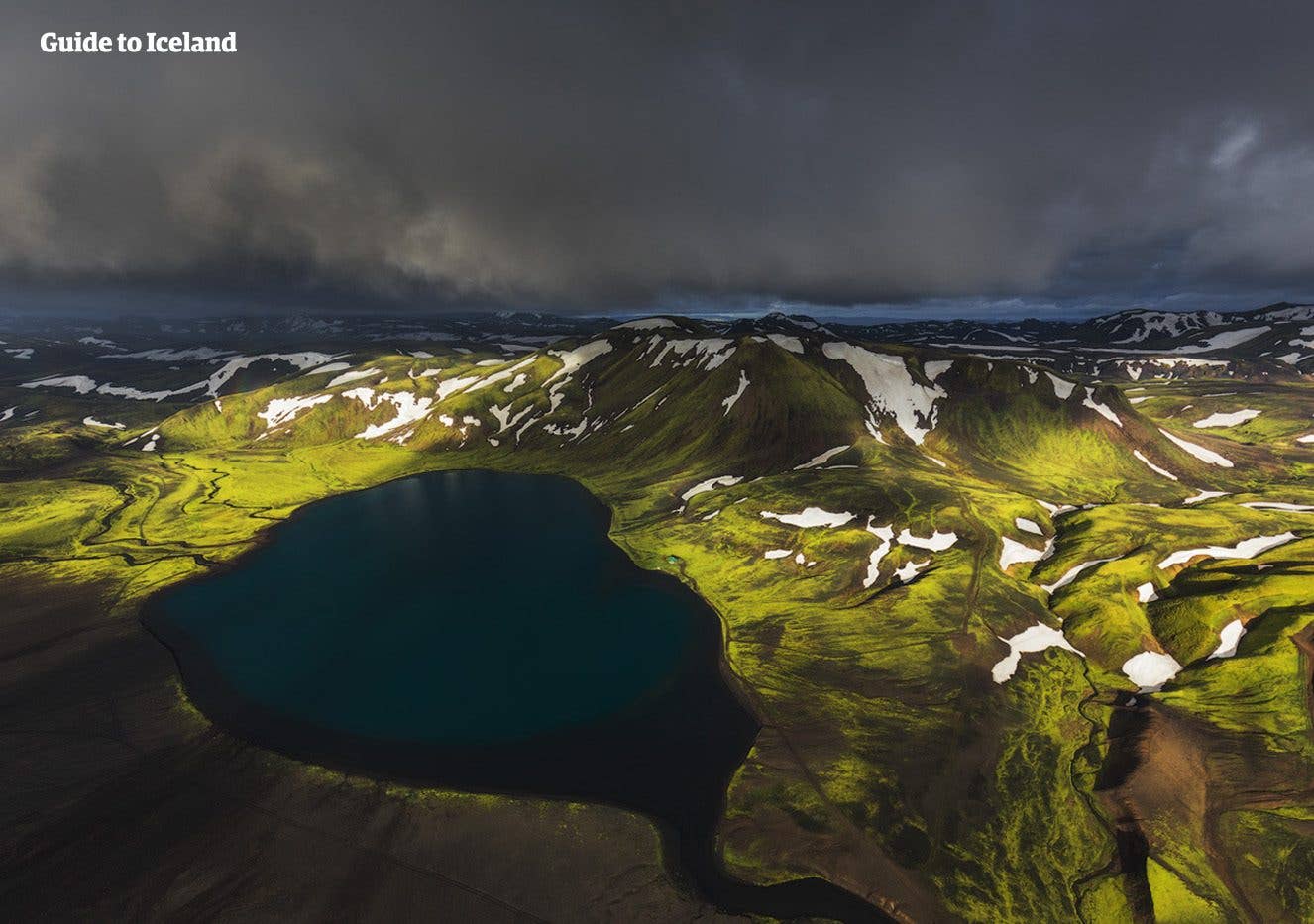 A deep blue crater lake sits among green Highland hills in the interior of Iceland.