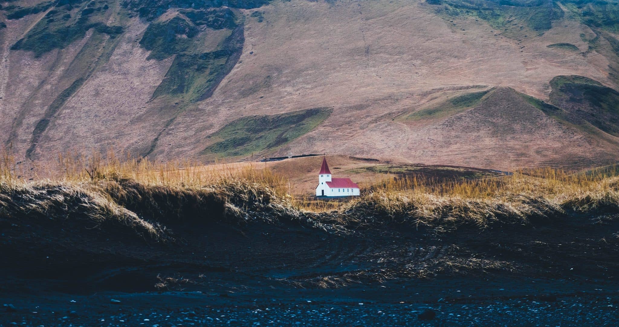 The small Reyniskirkja church sits on a green hillside above the black-sand coast near Vík in South Iceland.