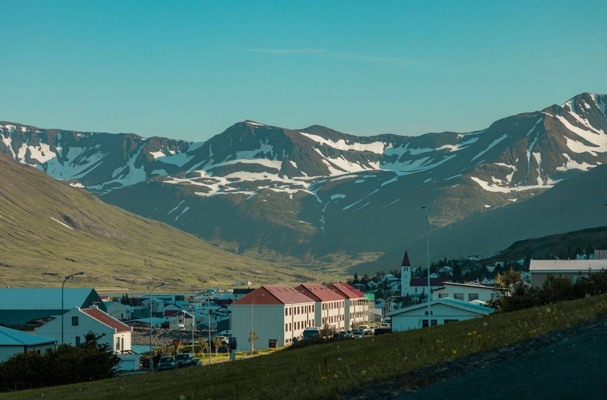 The church and colourful houses of Dalvík town sit below snow-streaked mountains in North Iceland.