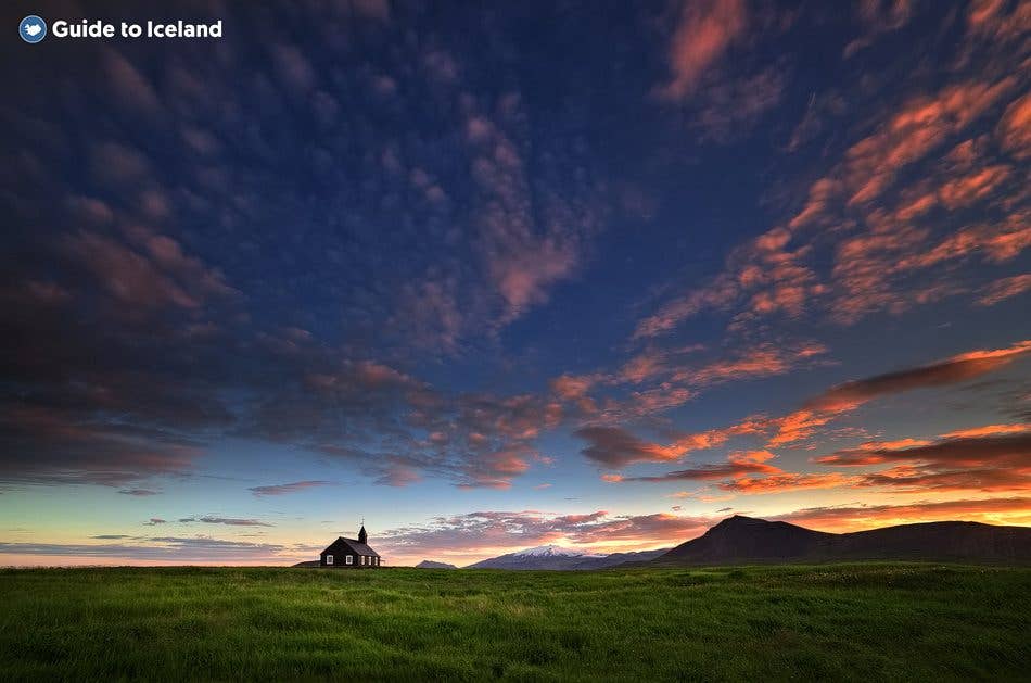 The black Búðakirkja church stands alone under a fiery sunset on the Snæfellsnes Peninsula, West Iceland.