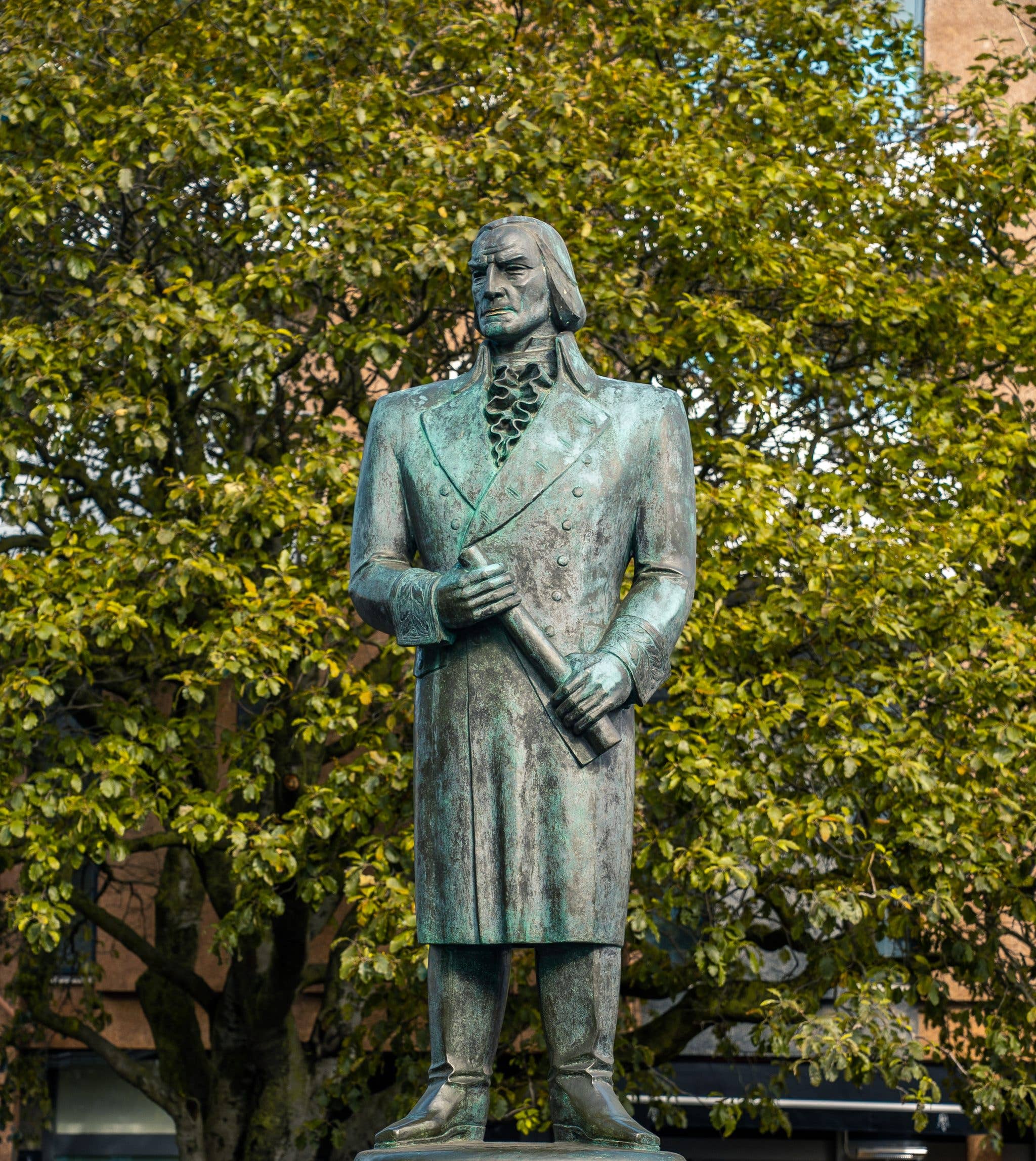 A bronze statue stands among trees in a leafy square in central Reykjavík, Iceland.