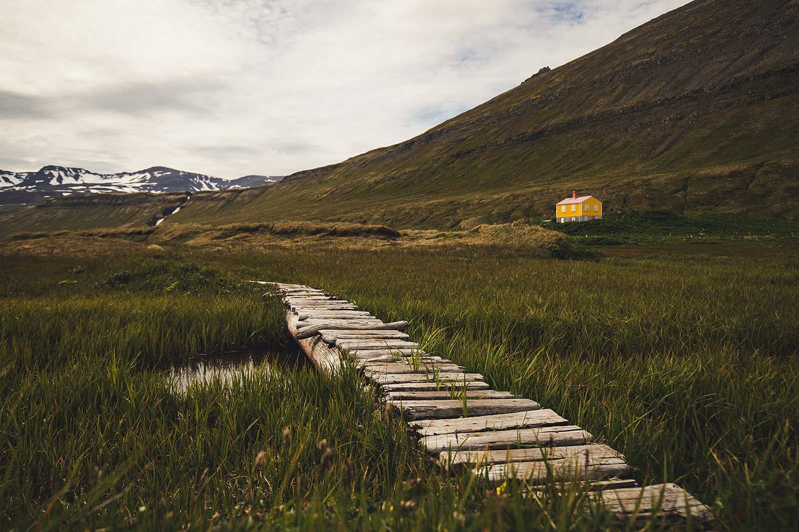 A boardwalk path crosses wetland toward the mountains of the Hornstrandir nature reserve in the Westfjords, Iceland.