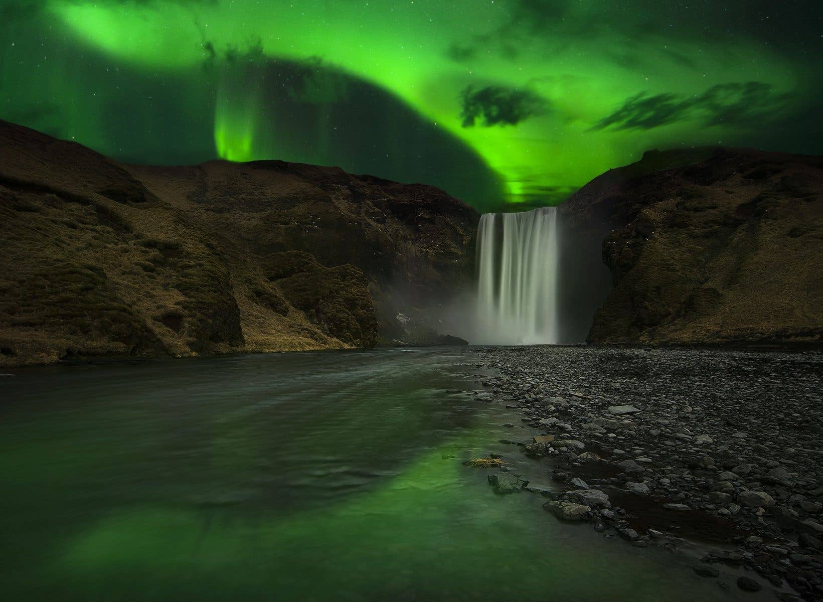 The northern lights glow above the powerful Skógafoss waterfall on the south coast of Iceland.