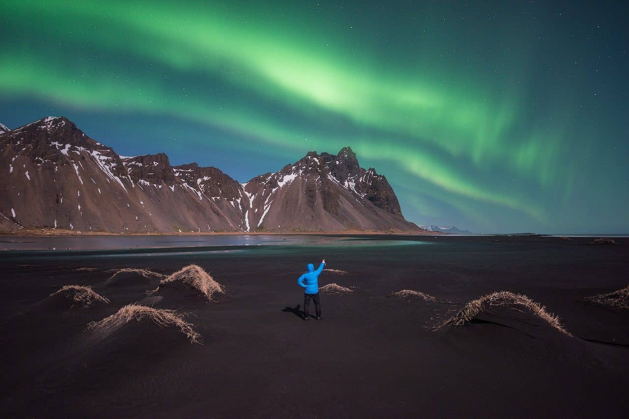 A traveller stands beneath the aurora before Vestrahorn mountain at Stokksnes in Southeast Iceland.